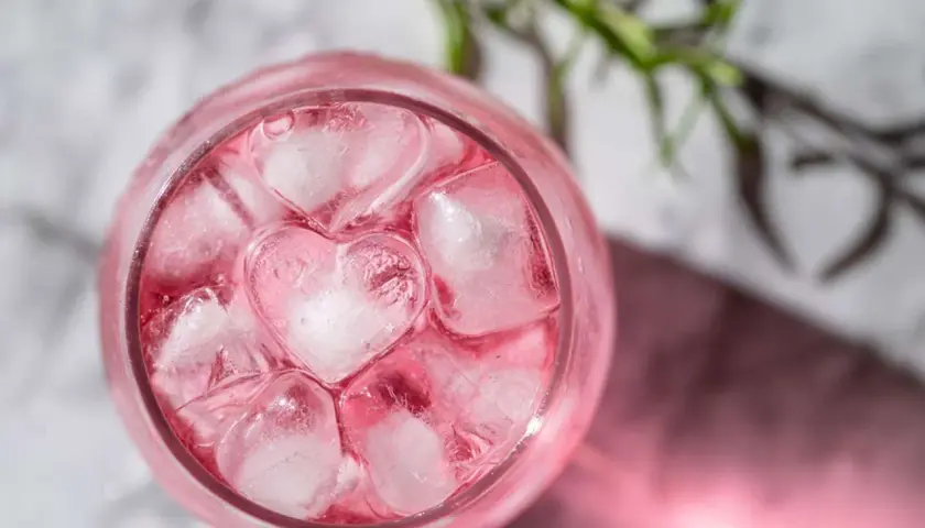En rosa drink med hjärtformade isbitar och en rosmarinkvist.