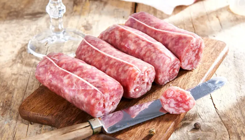 Frische Salsiccia-Würste auf Holzbrett, Messer mit Scheibe. Die korrekte Salsiccia Aussprache ist wichtig für den Genuss.