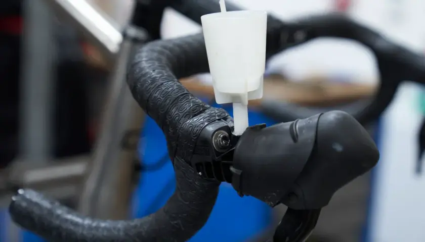 A white funnel attached to a bicycle handlebar, part of an easy way to bleed brakes.