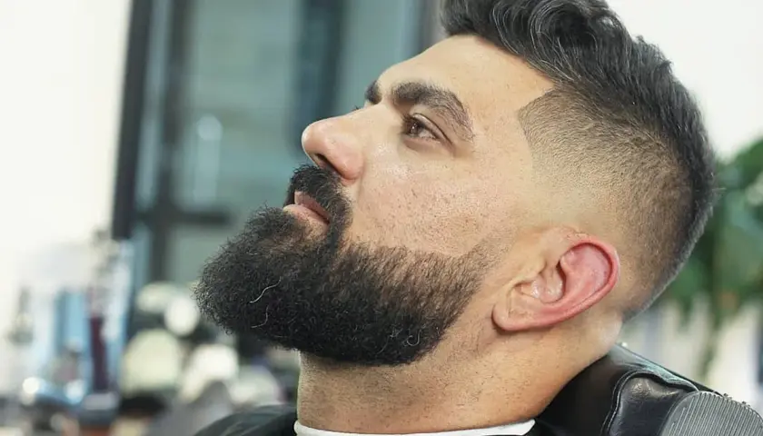 Hombre con barba y un moderno corte de pelo con degradado, uno de los tipos de corte de pelo hombre más populares.