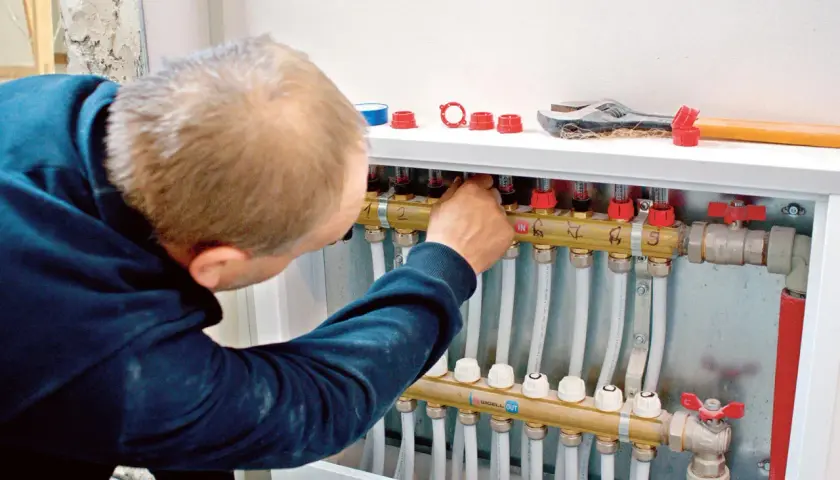 Instalator reguluje rozdzielacz ogrzewania podłogowego. To kluczowy etap, by przerobić grzejnik na ogrzewanie podłogowe.