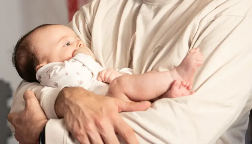 Dziecko trzymane w ramionach, z główką opartą o ramię, może sugerować źle noszenie niemowlaka. Jego nóżki swobodnie zwisają.