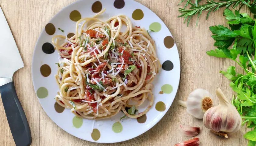 Un plato de espagueti aglio olio peperoncino, con ajo, perejil y un toque de tomate.