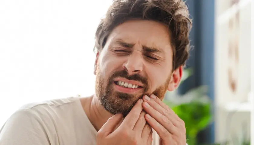 Hombre con expresión de dolor, tocándose la mejilla por una caries muela.