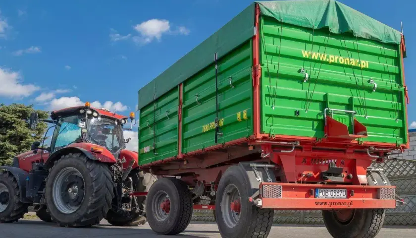 Czerwony traktor ciągnie zieloną przyczepę. Dowiedz się, jakich przyczep nie trzeba rejestrować, by ułatwić sobie pracę w gospodarstwie.