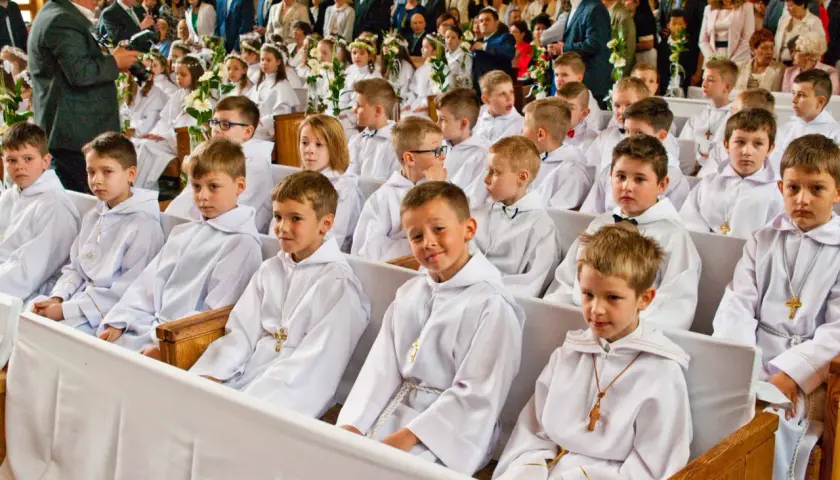 Dzieci w bieli na komunii świętej. Czy rocznica komunii jest obowiązkowa? Rodzice i goście obserwują uroczystość.