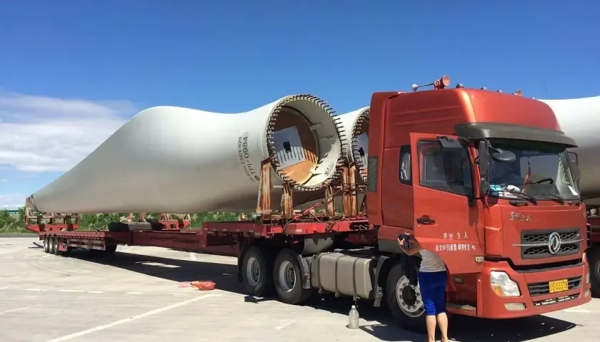 Ciężarówka transportuje łopatę turbiny wiatrowej. To ważny element w kraju tranzytowym, czekający na dalszą podróż.