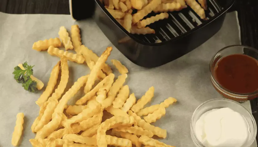 Frites maison ondulées, croustillantes et dorées, tout juste sorties de l'airfryer Ninja. Servies avec ketchup et mayonnaise.