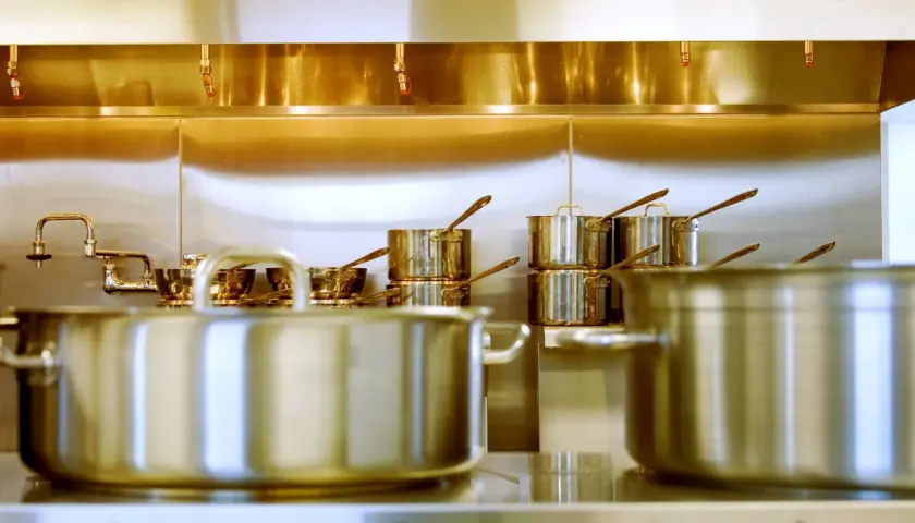 Une cuisine professionnelle avec des casseroles en inox 18/0 étincelantes sous une hotte aspirante.