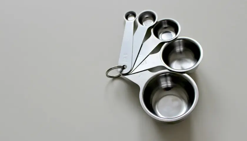 Zestaw metalowych miarek kuchennych o różnych rozmiarach, ułożonych na jasnym tle.