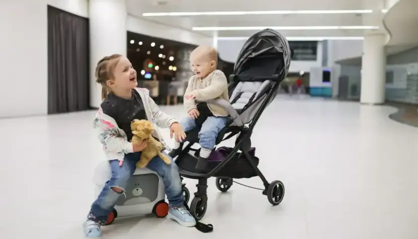 Dwie dziewczynki, jedna siedzi na walizce, druga w wózku, gotowe na podróż z Ryanair. Wózek dla 3 latka idealny na lotnisko.