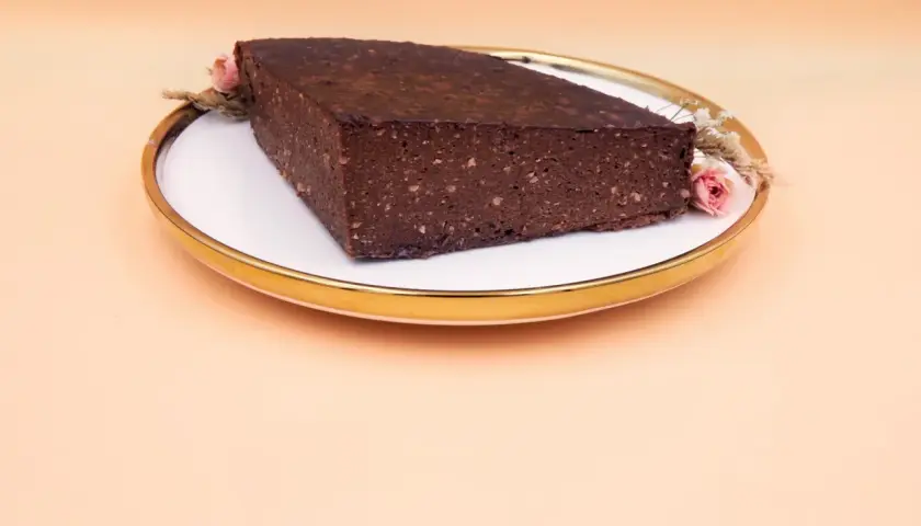 Czekoladowy brownie z bananami i masłem orzechowym, ozdobione suszonymi kwiatami, na talerzu ze złotym rantem.
