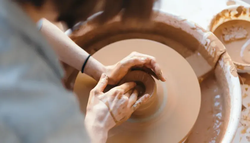 Dłonie artysty formują glinę na kole garncarskim. Powstaje piękna, ręcznie robiona pottery.
