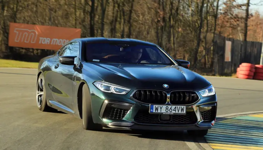 Mocne m8 bmw w ciemnozielonym kolorze na torze wyścigowym, z widocznym banerem "TOR MODLIN" w tle.