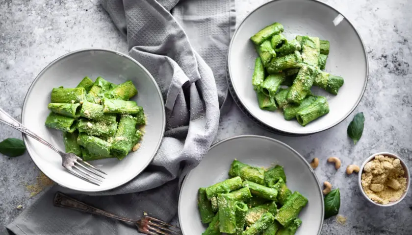 Drei Teller mit Rigatoni in cremiger, grüner veganer Spinatsoße, bestreut mit veganem Parmesan. Ein Genuss für Augen und Gaumen!