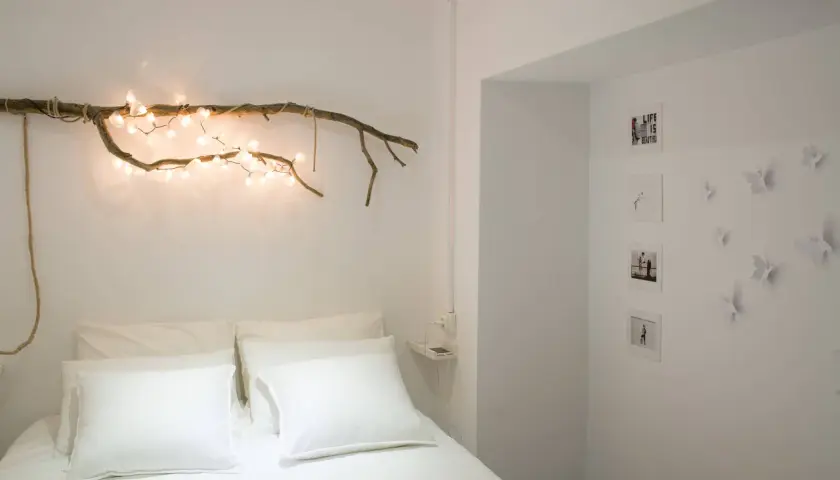 Ideas para decorar ramas secas: una rama con luces cálidas sobre la cama, fotos y mariposas en la pared.