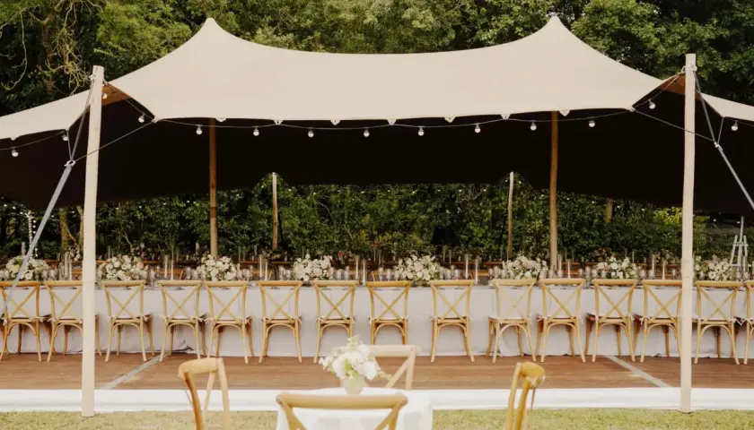 Une réception de mariage sous tente, avec des tables dressées et des chaises en bois. Un travail de cout wedding planner pour un événement mémorable.
