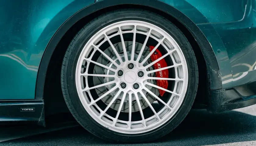 Detailaufnahme eines Autos mit auffälliger roter Bremsanlage. Der **Bremskolben fest** im Sattel deutet auf eine sportliche Performance hin.