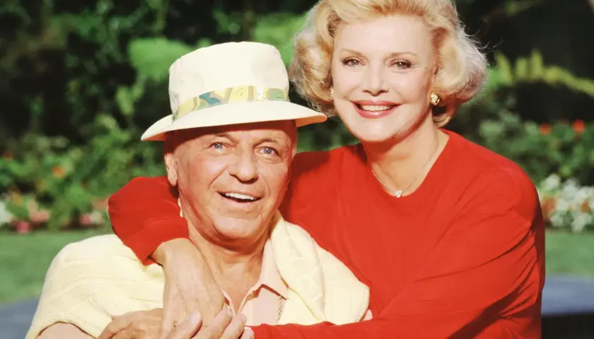 Frank Sinatra z żoną Barbarą, uśmiechnięci, w słoneczny dzień na tle zieleni.