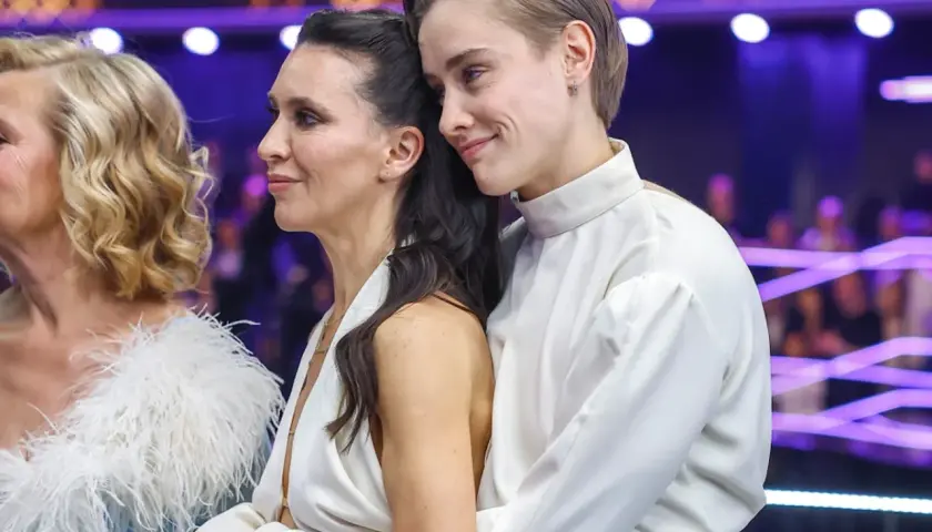 Katarzyna Zillmann i jej partnerka w białych strojach, czule objęte, na tle fioletowych świateł.