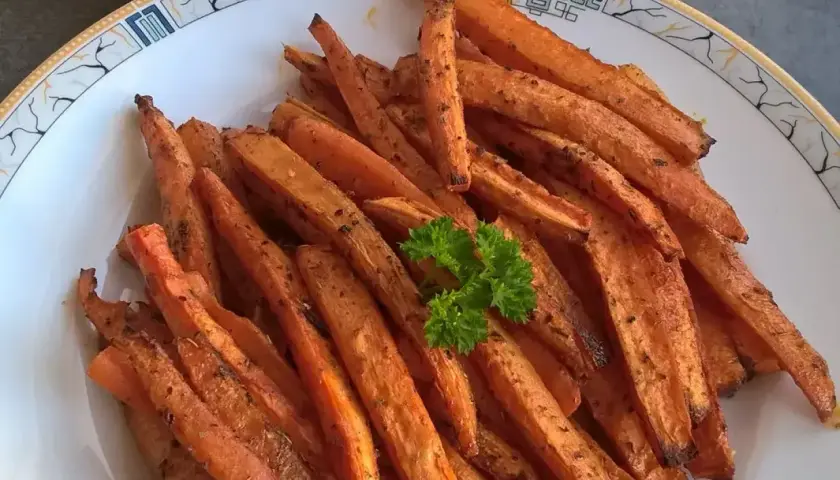 Chrupiące frytki z marchewki, przyprawione i lekko przypieczone, podane na talerzu z natką pietruszki.