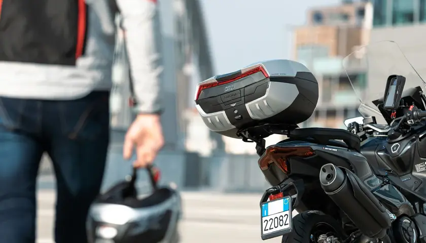 Hombre con casco en mano, listo para llevar su maleta en moto. La moto tiene un top case Givi Maxia.