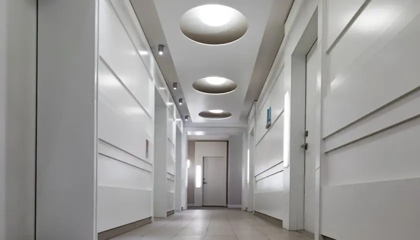 Nowoczesny pomysł na oświetlenie korytarza: okrągłe wpuszczane lampy w suficie i dyskretne kinkiety tworzą przytulną atmosferę.