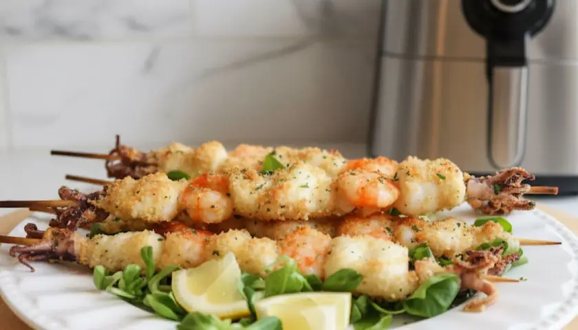 Spiedini di gamberi e calamari impanati, cotti alla perfezione nella friggitrice ad aria. Serviti su un letto di insalata con spicchi di limone.