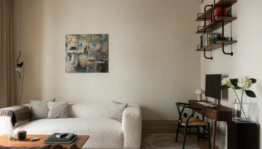 Soggiorno con divano bouclé bianco, tavolino in legno, quadro astratto e scrivania. Pareti color sabbia tortora chiaro RAL 1019.