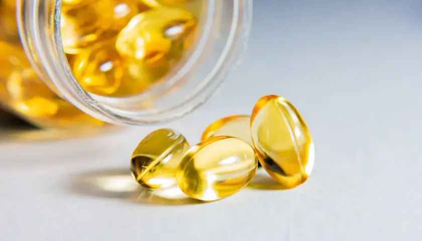 Żółte kapsułki z kwasy omega 3 wysypują się ze słoiczka.