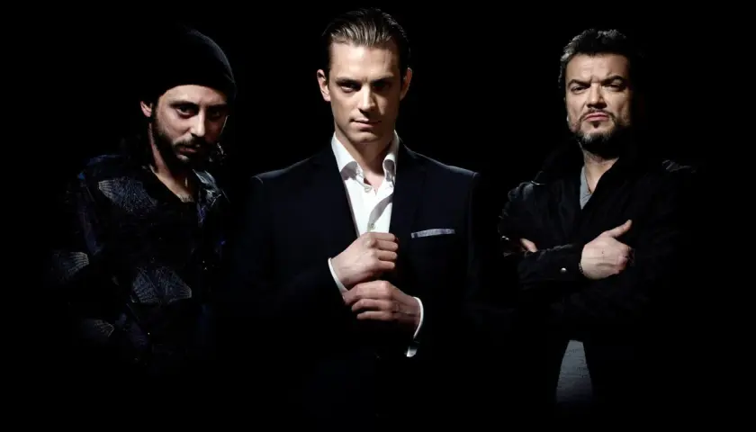 Tre män i mörka kläder poserar för snabba cash serie. En i kostym, en i jacka och en med mössa.