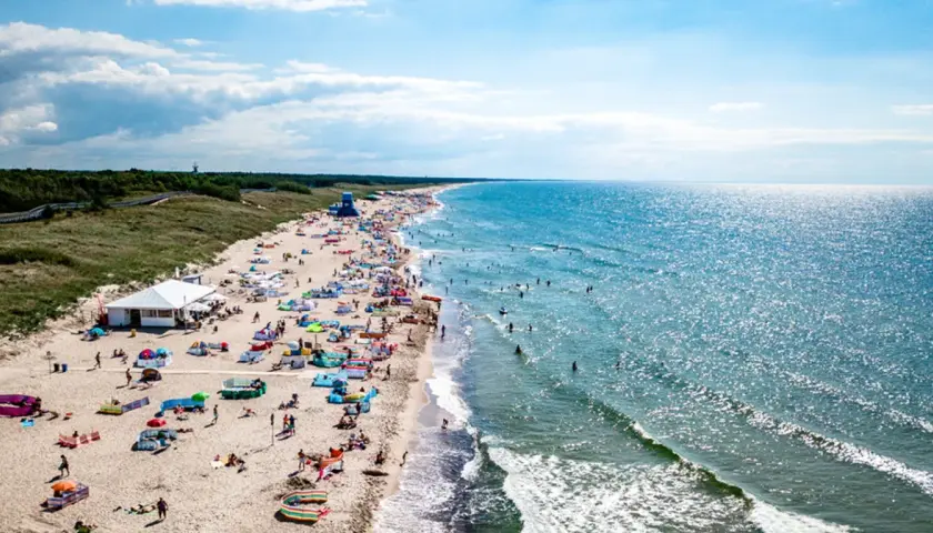Tłum ludzi na plaży w Darłowie, korzystających z uroków lata. Wiele kolorowych parawanów i namiotów, a w wodzie kąpielowicze. To wspaniałe darłowo atrakcje.