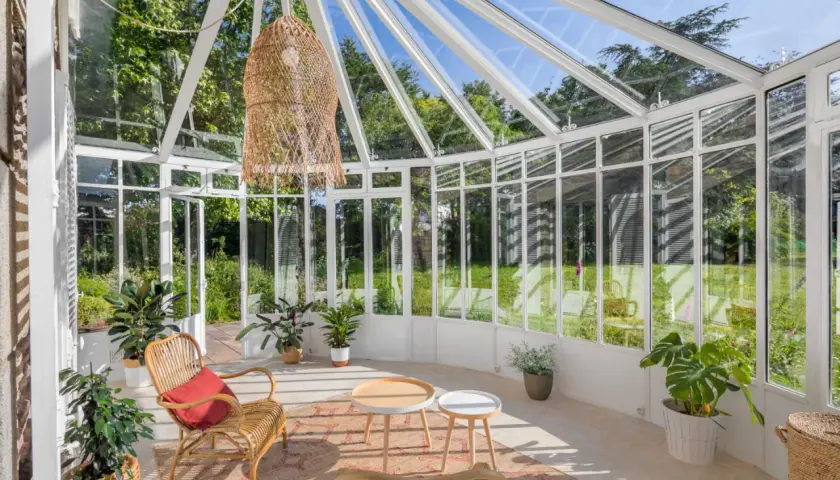 Une petite véranda cosy avec des meubles en rotin, des plantes vertes et une grande suspension en osier. Parfait pour un coin lecture paisible.