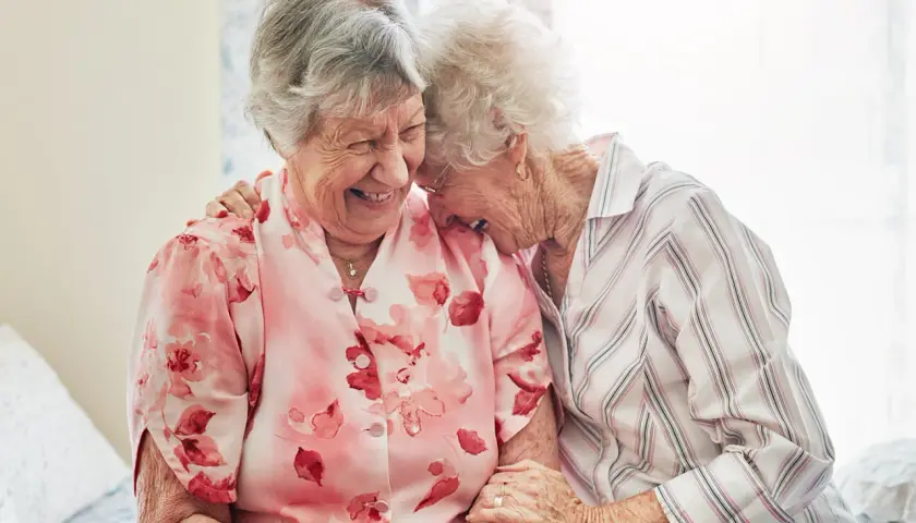 Zwei lachende Seniorinnen, die sich umarmen. Ein schönes Beispiel, wie man neue Freunde finden ab 60 kann.