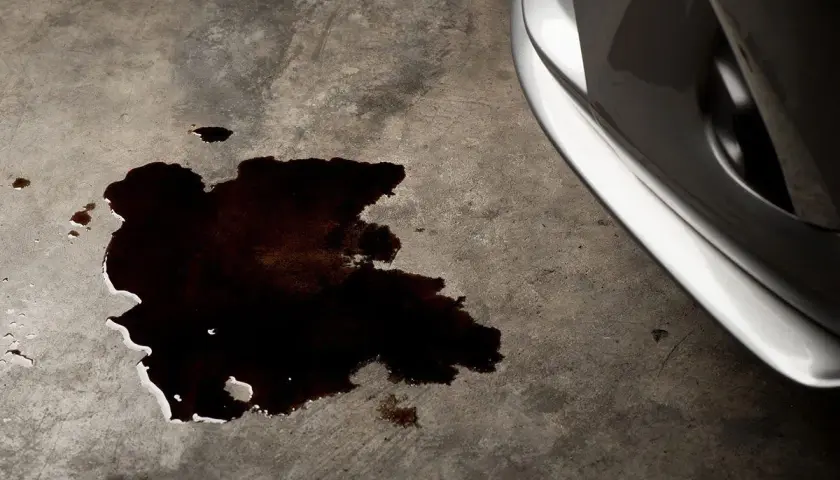 Mancha oscura de aceite en el suelo de hormigón, indicando una **pérdida de aceite del coche**.