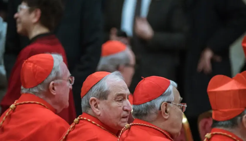Księża w czerwonych szatach i biretach, którzy mogą zostać kardynałem, siedzą w rzędzie.
