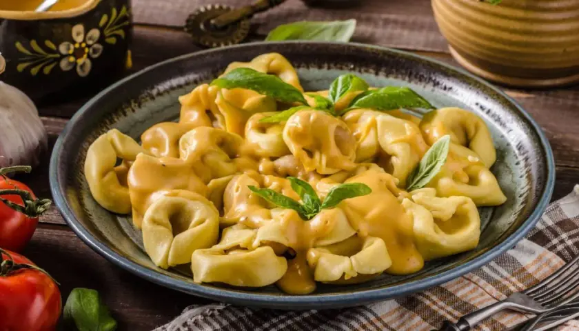 Plato de tortellini de carne cubiertos con una cremosa salsa de queso y decorados con hojas de albahaca fresca.