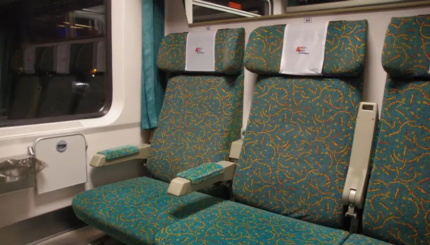 Wagon przedziałowy PKP Intercity. Korytarz z siedzeniami w turkusową tapicerkę z żółto-czerwonym wzorem.