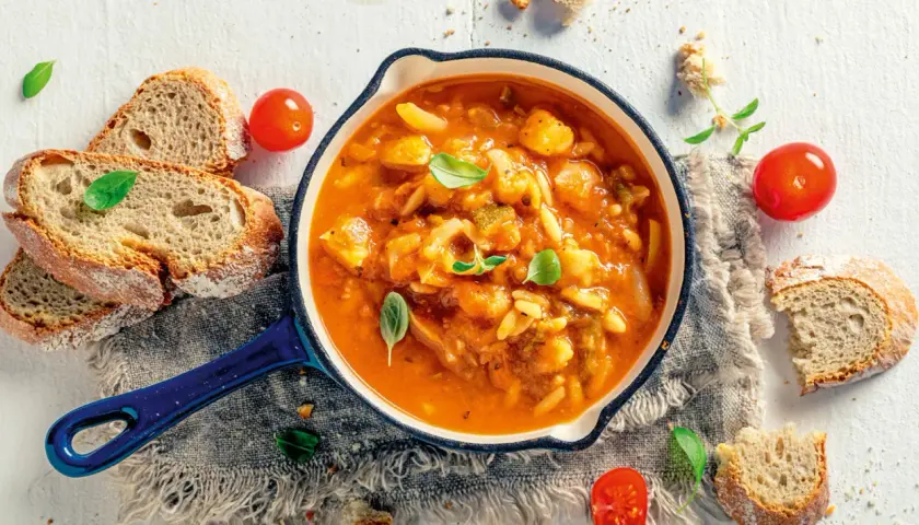 Eine dampfende, traditionelle italienische Suppe mit Gemüse und Pasta, serviert mit frischem Brot und Tomaten.