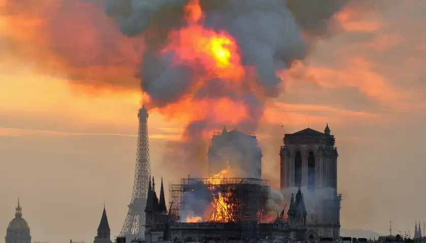 Płonąca katedra Notre-Dame w Paryżu z Wieżą Eiffla w tle.