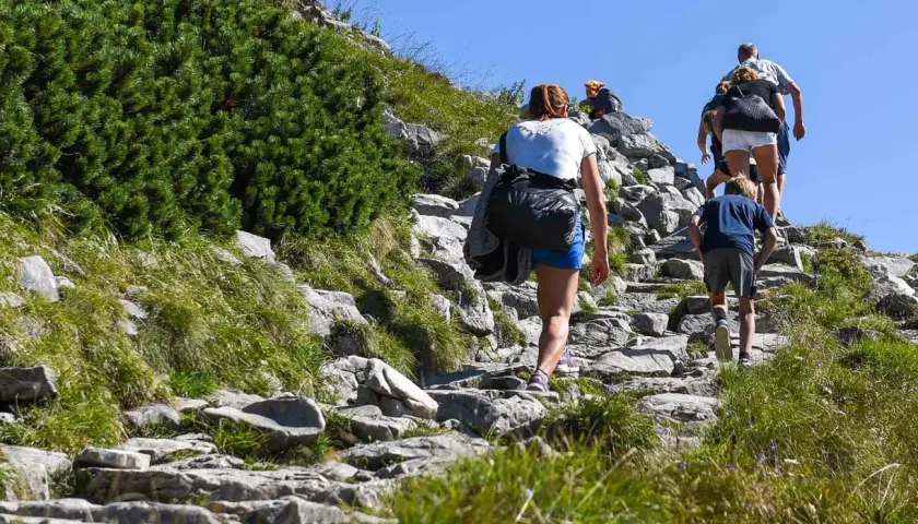 Rodzina wspina się kamienistym szlakiem. Dziecko idzie z przodu, a za nim dorośli. To ich wejście na Giewont.