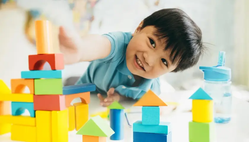 Niño sonriente jugando con bloques de colores, creando torres y casas. Perfectos juegos niños 3 años en casa para la imaginación.