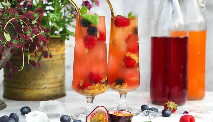 Två glas med fruktiga drinkar, fyllda med bär och passionsfrukt. Perfekt för en somrig bål med bubbel.