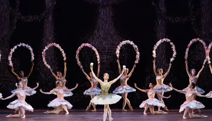 Balettdansöser i ljusa dräkter utför en scen från "Le Corsaire", med blomsterkransar i händerna.