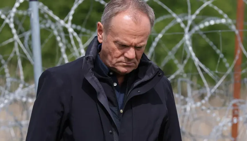 Mężczyzna w ciemnej kurtce patrzy w dół, za nim drut kolczasty. Czy to symbol jego hipokryzji?