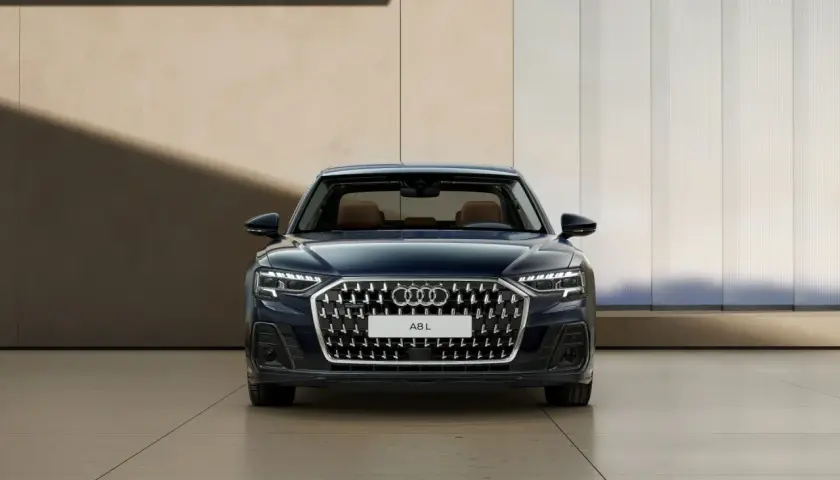 Elegancki, ciemnoniebieski Audi A8 2025 z brązowym wnętrzem prezentuje się na tle nowoczesnej architektury.