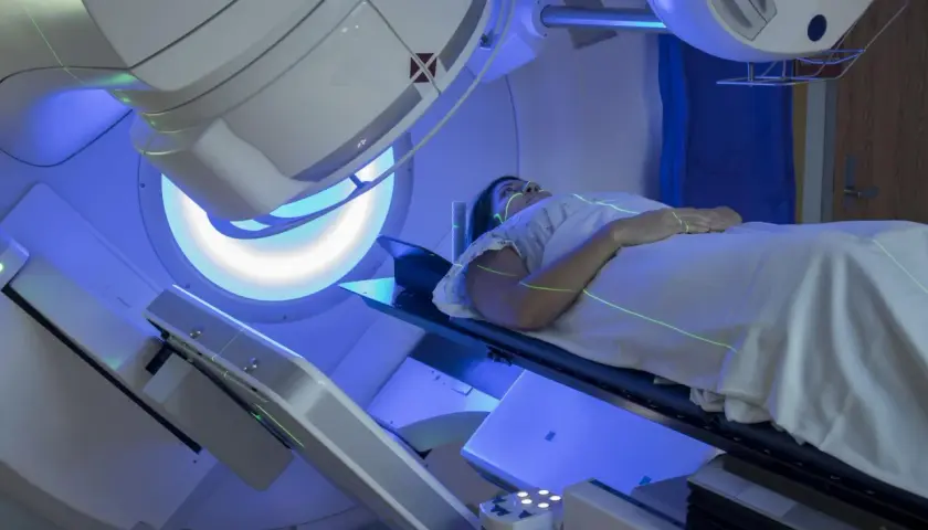 Kobieta leży na stole zabiegowym podczas radioterapii. Zielone linie lasera wyznaczają pole napromieniania.