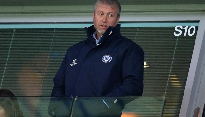 Roman Abramowicz w kurtce Chelsea FC, z emblematem Ligi Mistrzów, ogląda mecz z trybun.