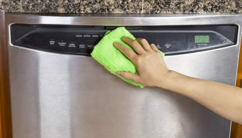 Mano limpiando un lavavajillas de acero inoxidable con un paño verde. Aprende como limpiar el acero inoxidable para mantenerlo brillante.