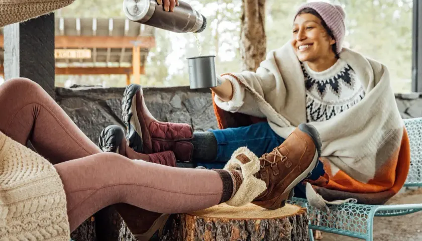Cozy friends share drinks outdoors, their feet snug in warm shoes to keep feet warm.